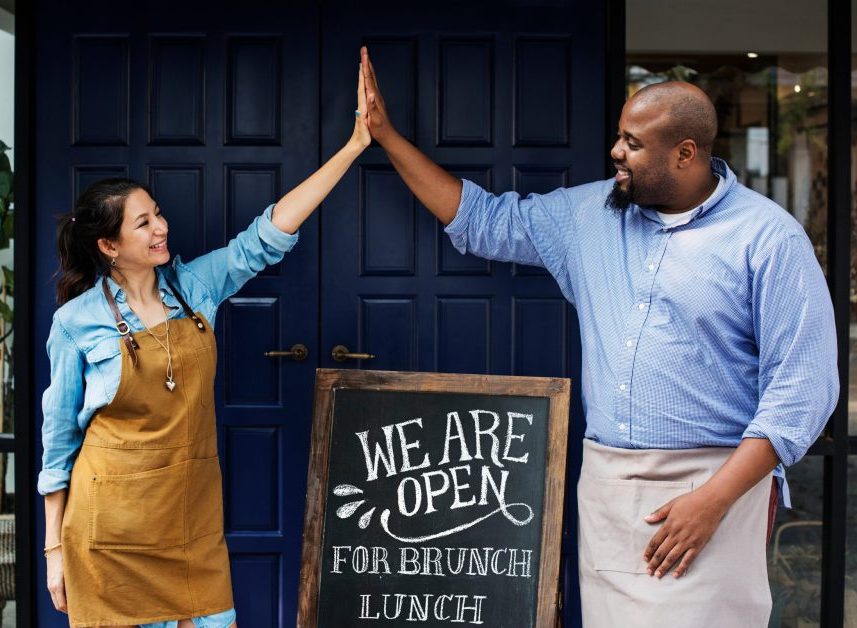 Cheerful business owners standing with open blackboard