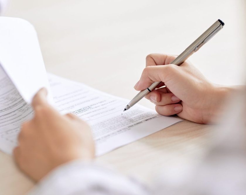 Crop shot of person with pen signing contract at desk in daylight