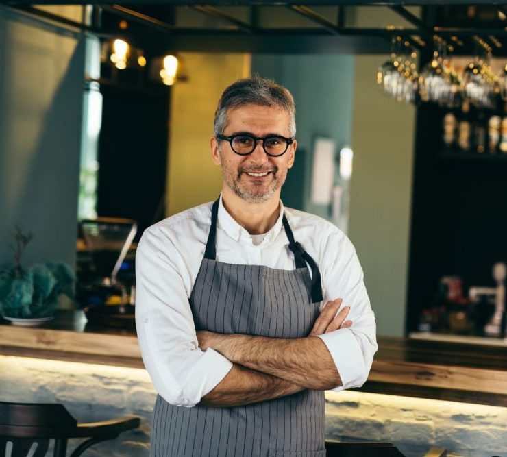 senior barman crosses arms standing in front of counter in cafe bar